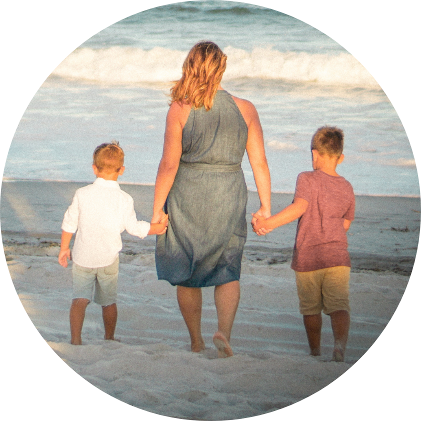 Blonde mother walking hand in hand with two small boys in beach sand